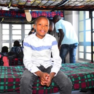 Boy sitting on the bottom bunk bed with other boys on the bed behind